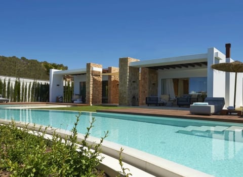 Modern minimalist house with turquoise pool, brick and white elements, surrounded by green landscaping under clear blue sky
