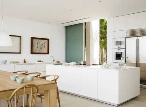 Modern kitchen with white cabinetry, wood dining table, stainless steel appliances, and green accent wall
