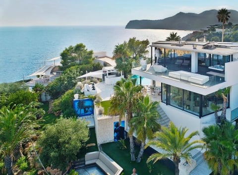 Aerial view of modern luxury beachfront villa with white architecture, palm trees, and turquoise Mediterranean sea view