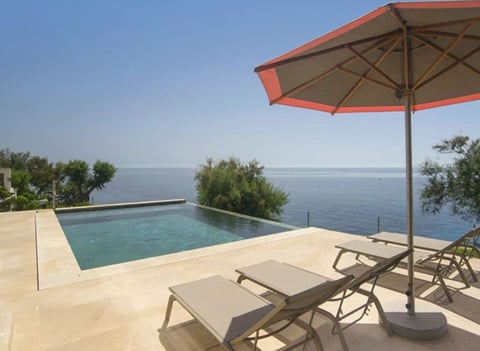 Luxury infinity pool overlooking the sea with lounge chairs and red umbrella
