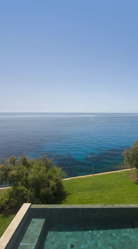 Infinity pool overlooking turquoise Mediterranean sea with green lawn