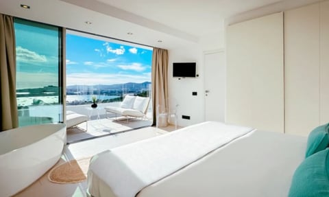 Modern hotel bedroom with large windows overlooking a coastal city skyline and bay with mountains