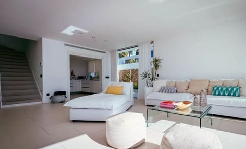 Modern open-plan bedroom and living area with white bed, beige sofa, glass coffee table