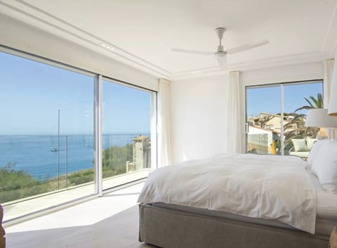 Modern bedroom with ocean view, white bed, and sliding glass doors