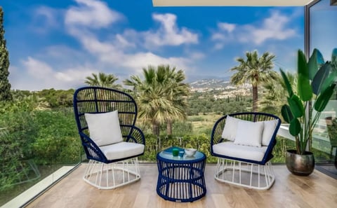 Modern outdoor patio with two navy wicker chairs, small side table, and potted plant overlooking palm trees and mountains