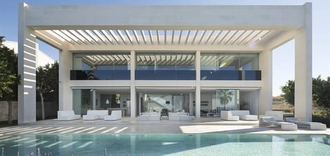 Modern white house with large glass windows and pergola roof overlooking a swimming pool