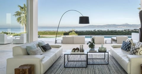 Modern living room with white sofas, arc lamp, and floor-to-ceiling windows overlooking coastal ocean view