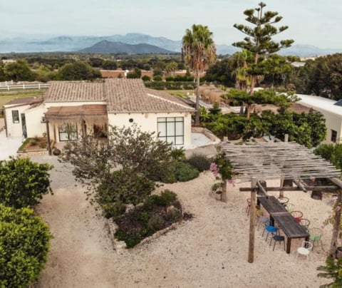 Aerial view of a modern desert home with terracotta roof, surrounded by landscaped gardens, palm trees, and mountains in the background