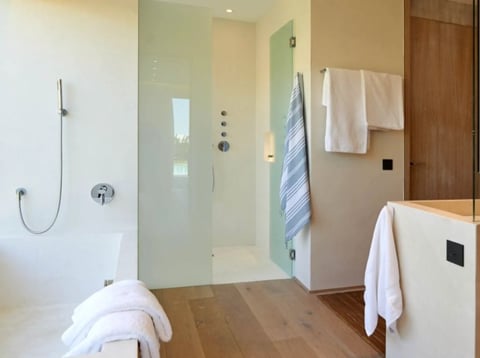 Modern bathroom with glass shower enclosure, wooden flooring, white vanity, and towel racks with soft furnishings