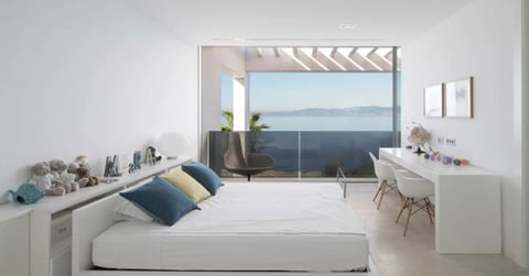 Modern minimalist bedroom with white bed, ocean view through large window, desk area