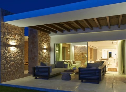 Modern patio with blue ceiling, stone columns, dark blue seating, and interior rooms visible through large glass doors