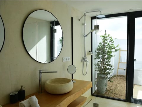 Modern bathroom with round mirror, cream vessel sink on wooden counter, glass shower