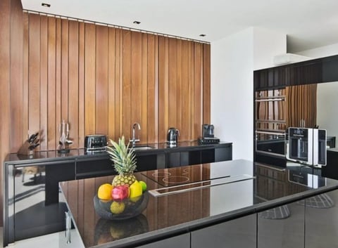 Modern kitchen with black countertops, wooden vertical cabinet panels, island with fruit bowl, and stainless steel appliances