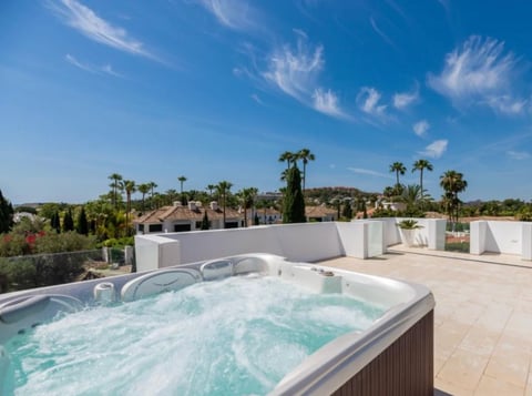 Rooftop hot tub with bubbling water overlooking a sunny residential area with palm trees and blue sky