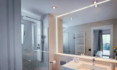 Modern bathroom with large illuminated mirror, double sinks, glass shower enclosure