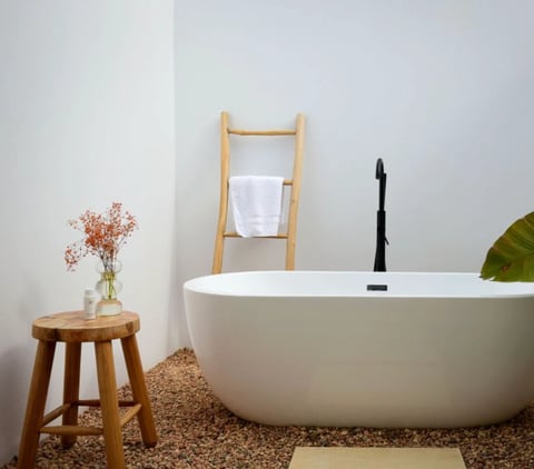 Modern white soaking tub in a minimalist bathroom with wooden stool and dried flowers