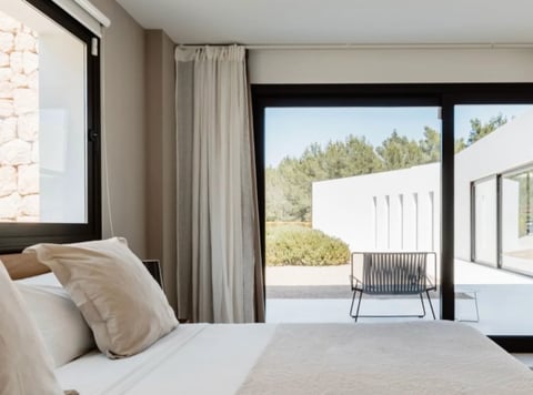Modern bedroom with floor-to-ceiling windows, beige pillows on white bed