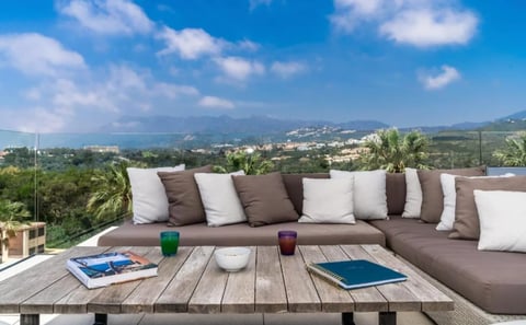 Outdoor terrace with sectional sofa, wooden table, and panoramic mountain valley view on a sunny day