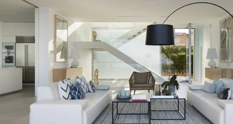 Modern open-plan living room with white sofas, arc floor lamp, coffee table, and staircase