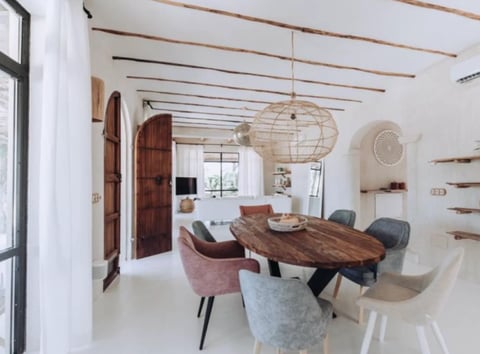 Modern dining room with wooden table, mixed upholstered chairs, woven pendant light, exposed wooden beams, and minimalist white walls