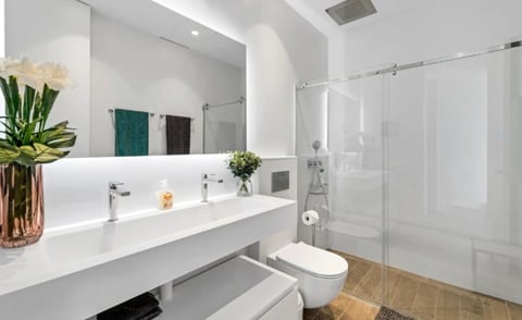 Modern bathroom with white floating vanity, glass shower enclosure, white toilet, and decorative flowers in a vase on the counter