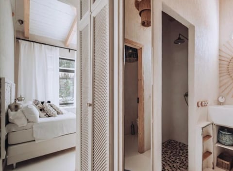 Modern minimalist bedroom with en-suite bathroom, featuring a bed with pillows, wooden partition screens, and a doorway leading to a shower room