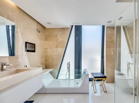 Modern luxury bathroom with white freestanding soaking tub, marble walls, double sink vanity, and floor-to-ceiling windows with city view