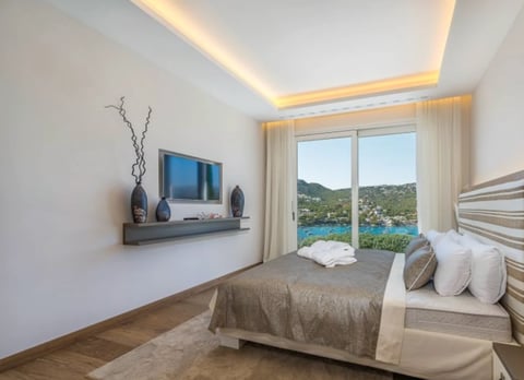 Modern luxury bedroom with wall-mounted TV overlooking scenic coastal landscape