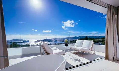 Modern rooftop terrace with white lounge chairs overlooking a coastal bay and mountains