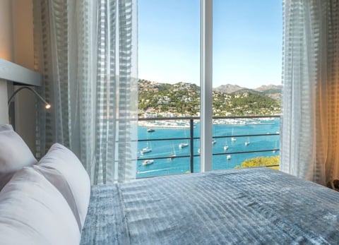 Luxury bedroom with floor-to-ceiling windows overlooking a coastal bay with sailboats