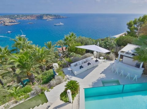 Luxury clifftop villa with turquoise pool, lounge area, and panoramic sea view with sailboats and islands
