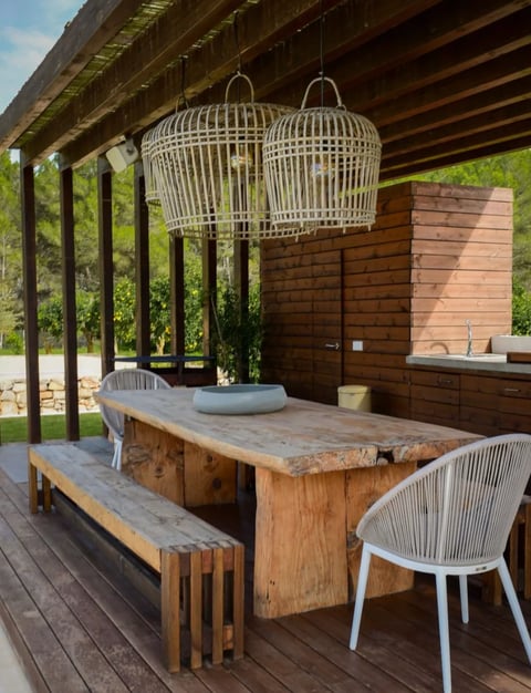 Modern outdoor patio with wooden dining table, white chairs, woven pendant lights