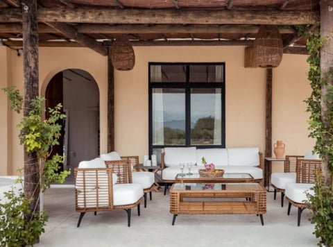 Contemporary outdoor patio with wooden furniture, white cushioned seating, and climbing ivy on cream-colored walls
