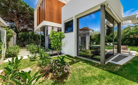 Modern white and wood house with large windows, green lawn, landscaping, and covered patio area under blue sky