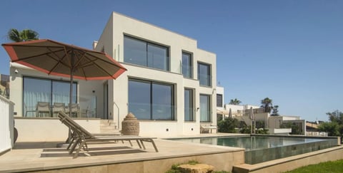 Modern white residential building with pool, lounge chairs, and red umbrella on patio