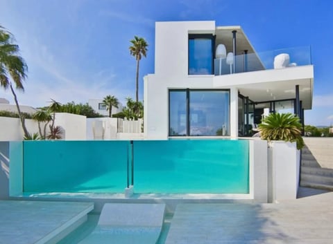 Modern white villa with turquoise pool and glass gates, palm trees, and blue sky