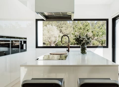 Modern kitchen with white cabinetry, large window overlooking greenery, island with seating