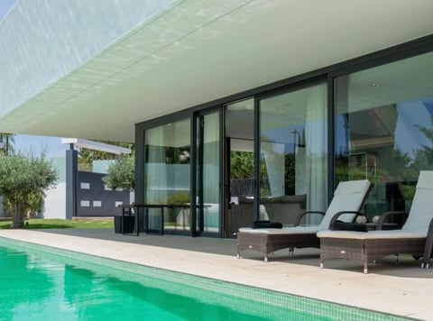 Modern pool house with glass doors, lounge chairs on terrace, and turquoise swimming pool in foreground