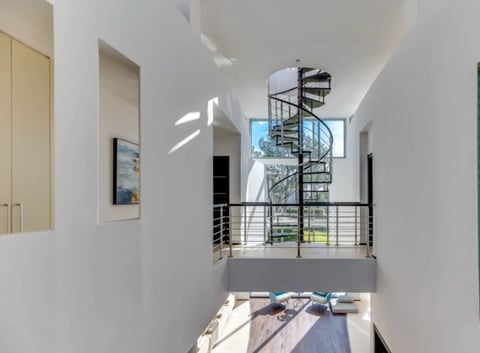 Modern interior with spiral staircase, metal railings, white walls, and natural light from windows in a multi-level space