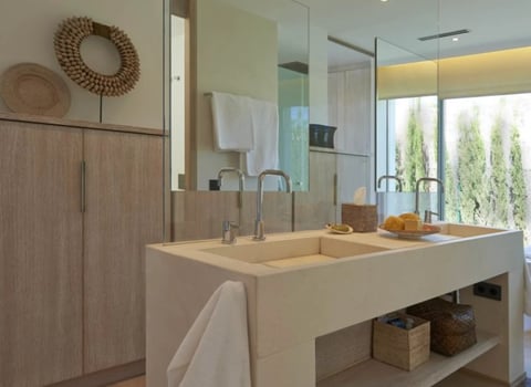 Modern bathroom with double concrete sink, wood cabinetry, large mirror, and bright natural light from glass doors