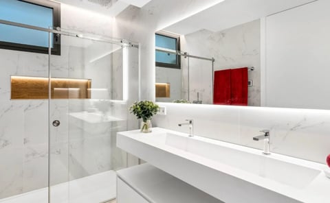 Modern bathroom with white marble walls, floating vanity with dual sinks, and glass shower enclosure with warm accent lighting