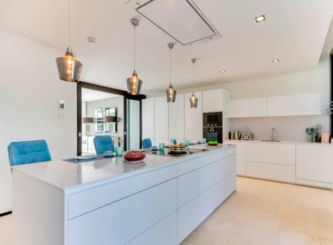 Modern white kitchen with a large island, blue pendant lights, and matching blue upholstered chairs