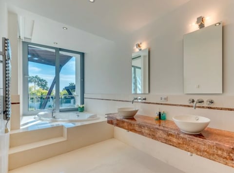 Modern bathroom with dual vessel sinks on wooden counter, soaking tub by window, and glass door leading to outdoor patio