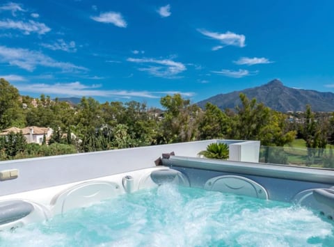 Hot tub with bubbling turquoise water on a rooftop terrace overlooking a mountain and green landscape